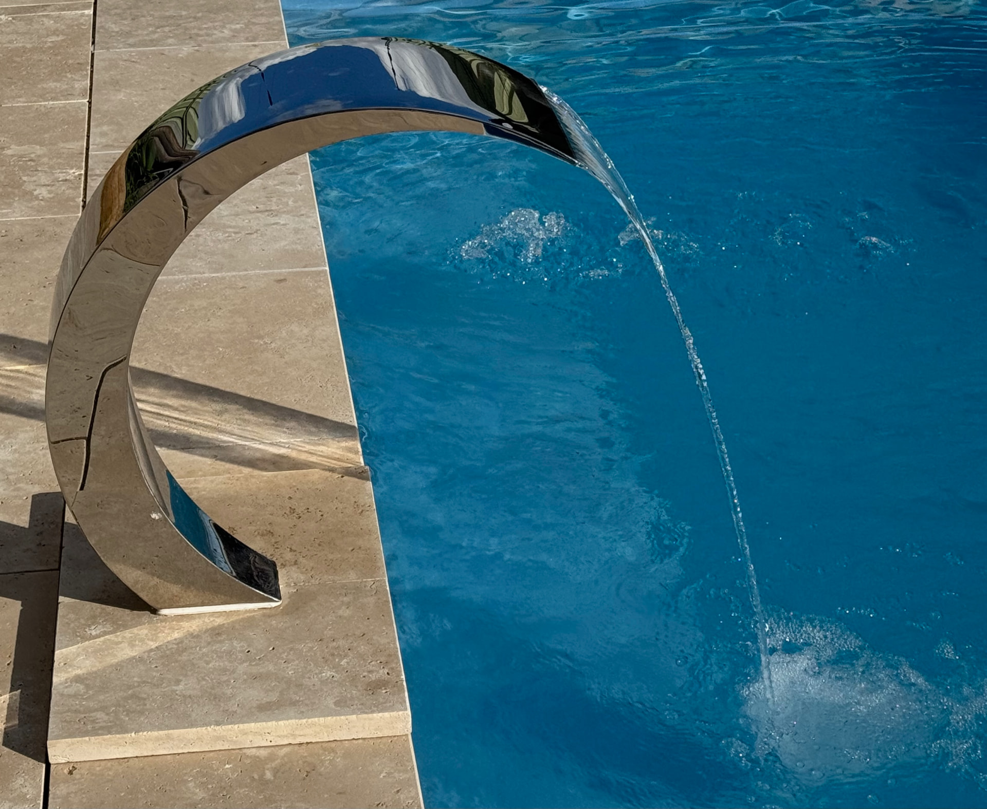 Mirror polished water arc feature at the edge of a blue pool