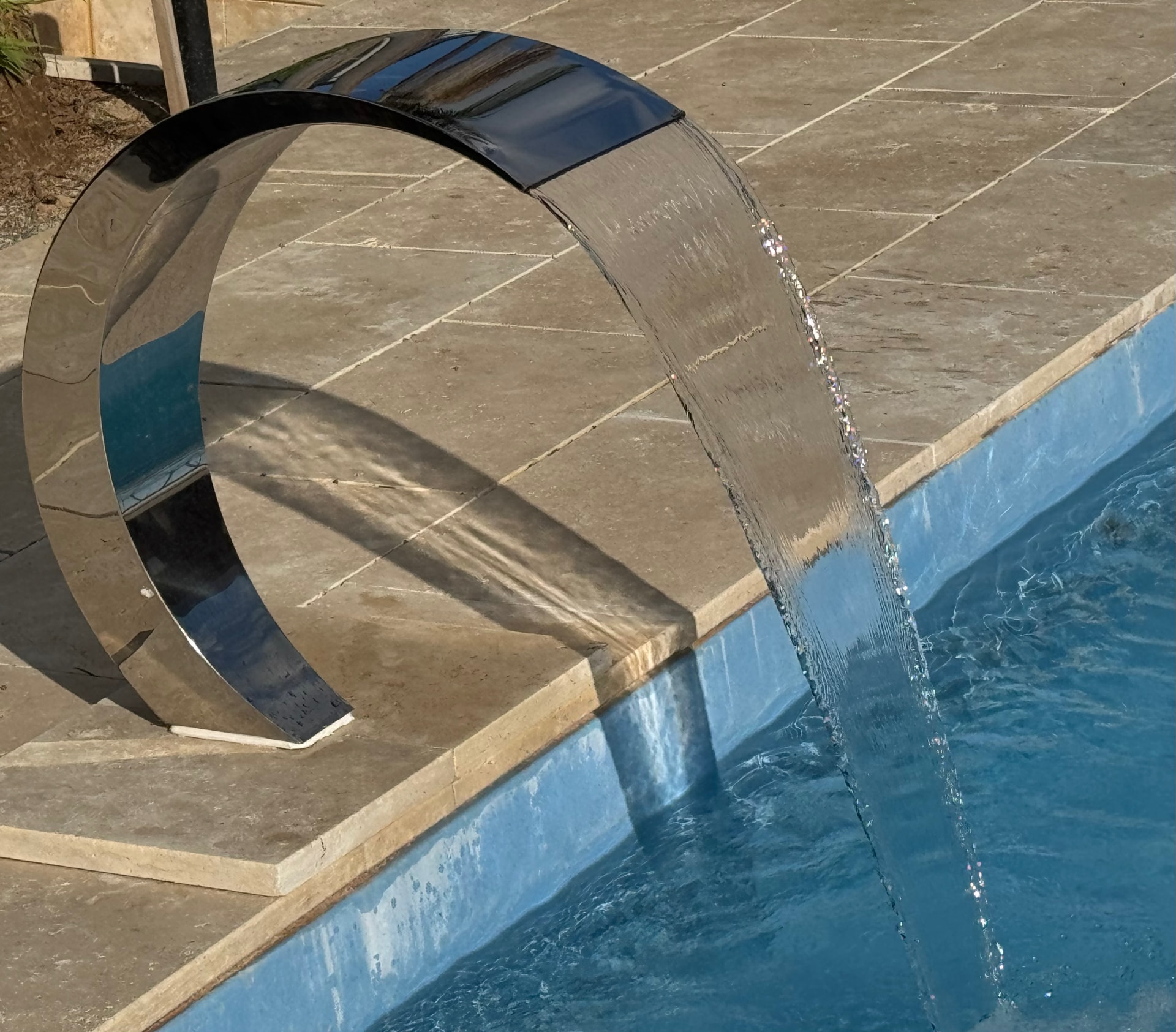 Polished stainless water blade arc pouring a sheet of water into the pool